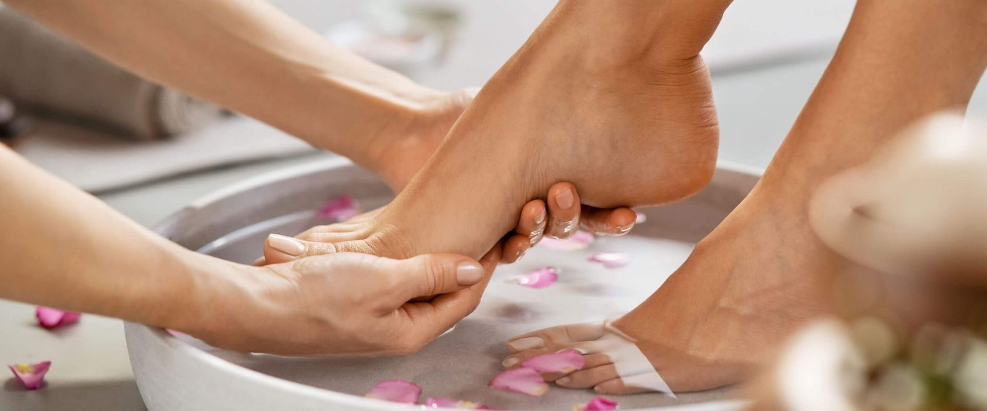 Eine entspannende Fußmassage wird in einem Kosmetikstudio mit Rosenblättern in einer Schüssel durchgeführt.