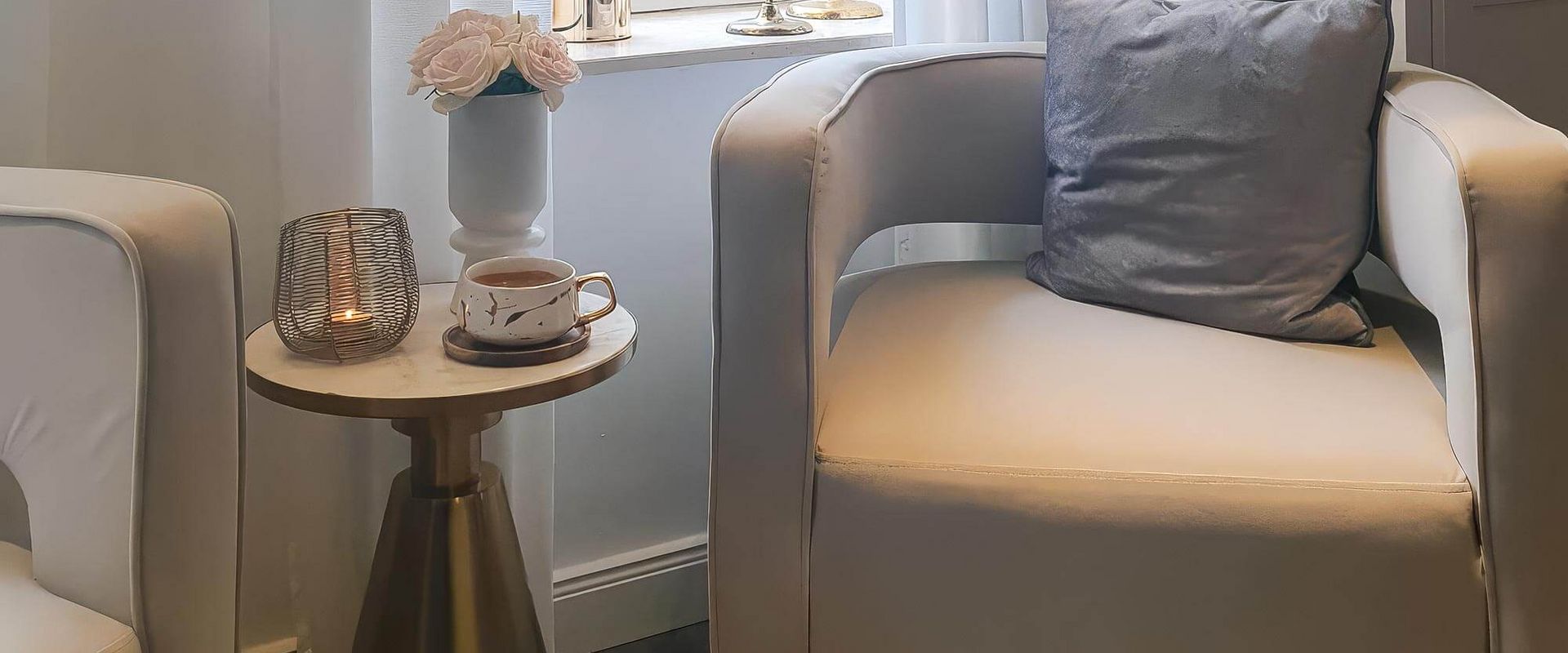 Ein gemütlicher Kosmetikstudio-Bereich mit stilvollen Sesseln, einer Tasse Tee und dekorativen Blumen am Fenster.