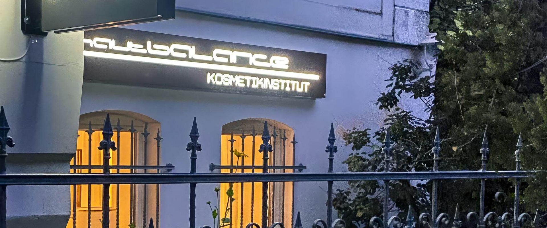 Das Kosmetikstudio Babor ist abends beleuchtet, während Pflanzen an der Fassade für eine einladende Atmosphäre sorgen.