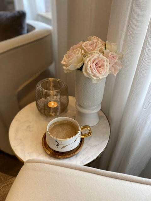 Ein stilvoller Tisch im Kosmetikstudio mit einer Tasse Kaffee, Rosenblüten und einer Kerze sorgt für entspannte Atmosphäre.