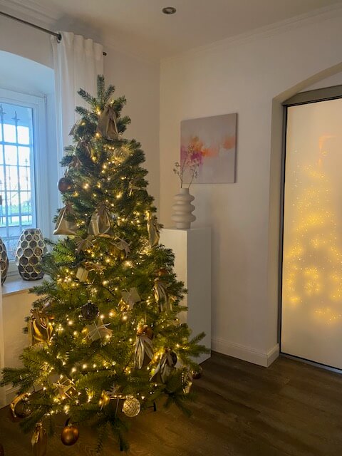 Ein festlich geschmückter Weihnachtsbaum mit Lichtern steht in einem eleganten Raum, der an ein Kosmetikstudio erinnert.