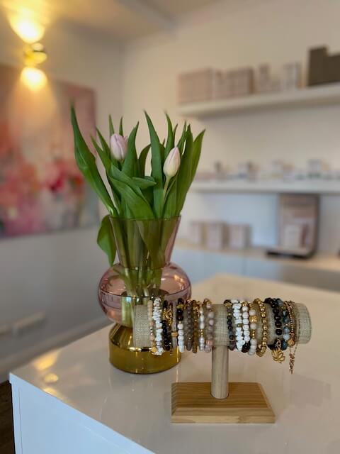 Ein elegantes Kosmetikstudio zeigt eine Vase mit Tulpen und ein Schmuckdisplay auf einem weißen Tresen.