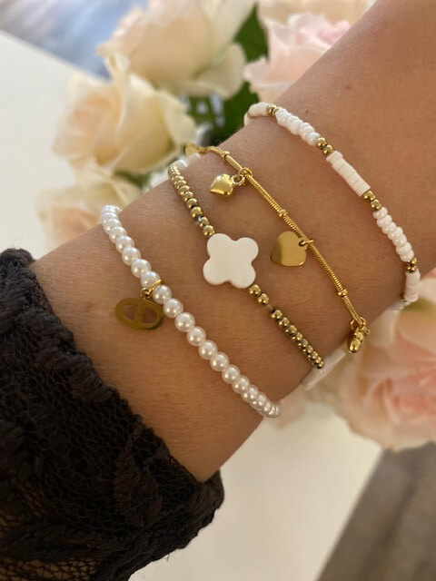 Elegante Armbänder schmücken ein Handgelenk, im Hintergrund zarte Blumen, wie in einem stilvollen Kosmetikstudio.