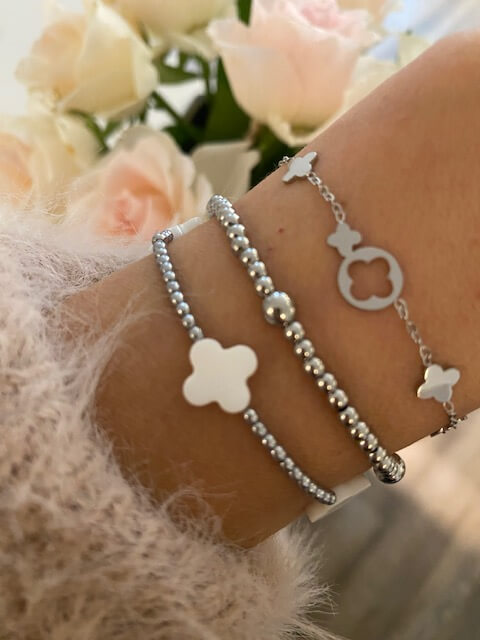 Elegante Armbänder mit Blumenmotiv schmücken ein Handgelenk vor einem Hintergrund aus zarten Rosen im Kosmetikstudio.