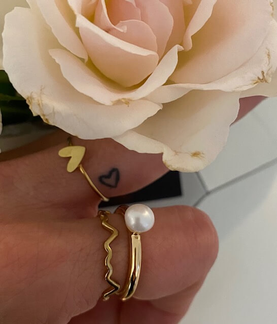 Eine Hand mit eleganten Ringen hält eine zarte Rose, perfekt für ein stilvolles Kosmetikstudio.
