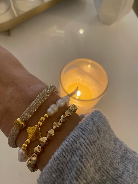 Ein Handgelenk mit eleganten Armbändern wird neben einer sanft leuchtenden Kerze in einem Kosmetikstudio gezeigt.