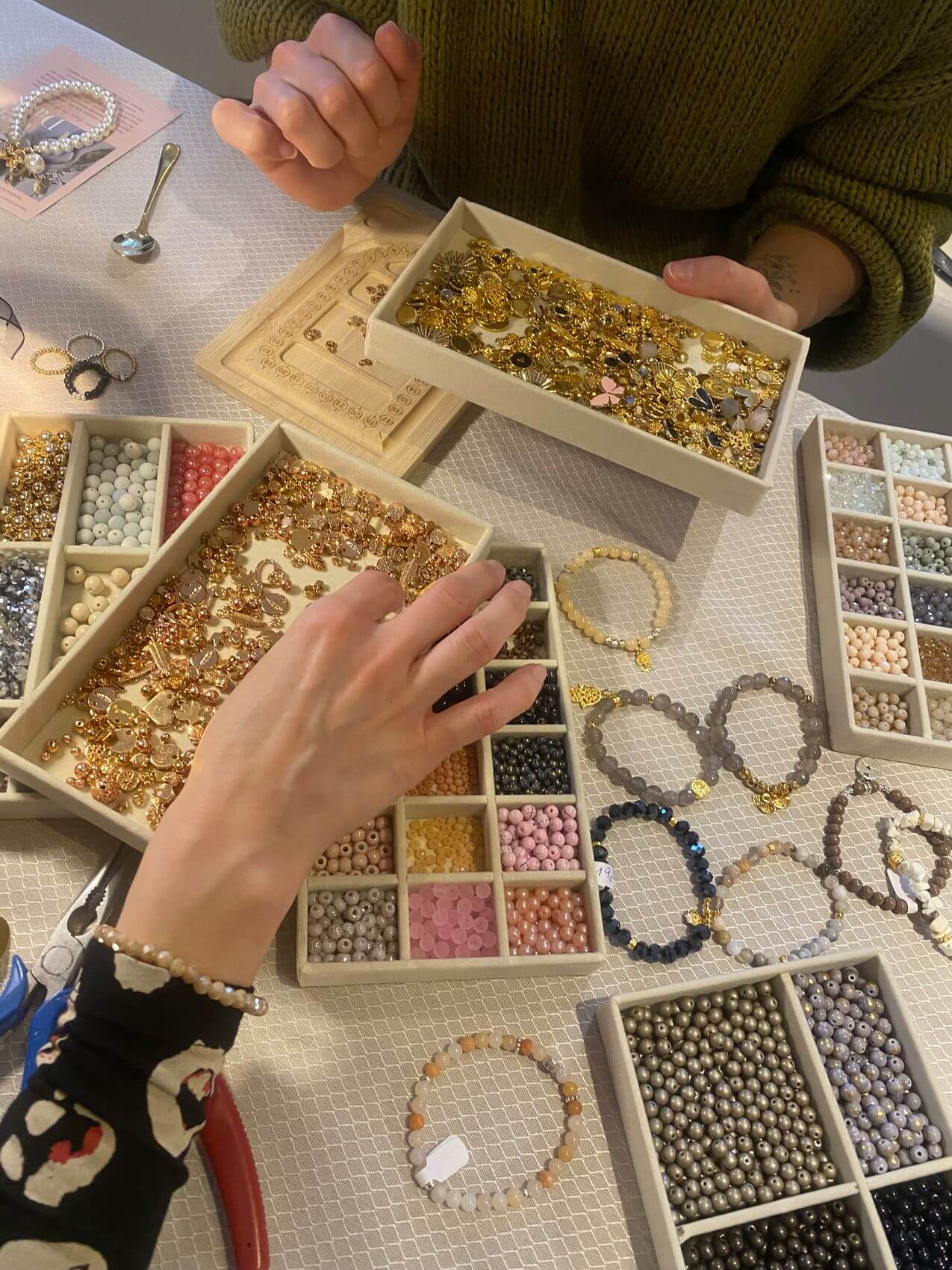 Zwei Personen kreieren im Kosmetikstudio Schmuck mit bunten Perlen und filigranen Details.